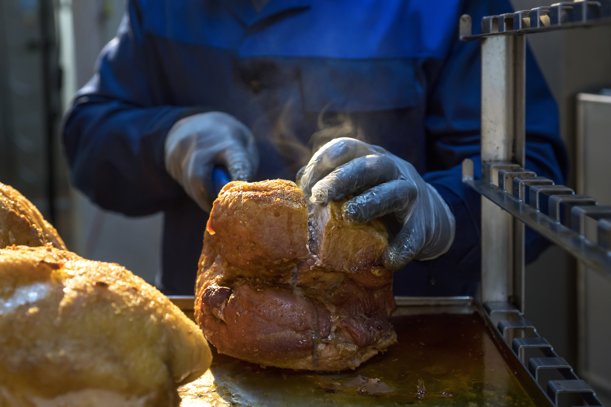 Worker at meat processing plant slices into a cut of cooked meat. Image courtesy of Getty Images.