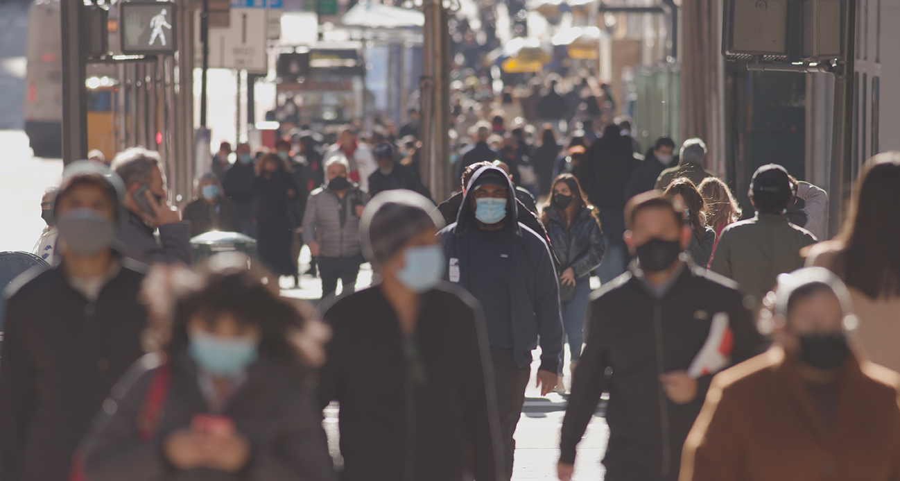 People in masks on a crowded urban street during the COVID-19 pandemic. Courtesy of Adobe Stock.