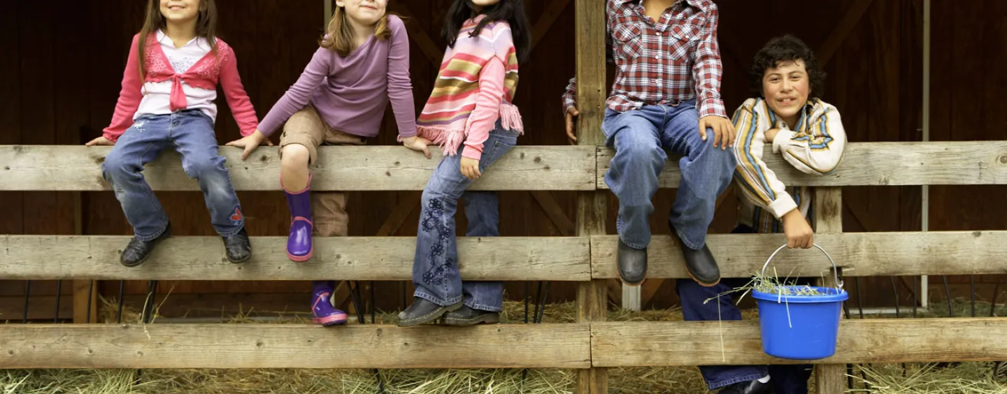 Kids on fence in barn. Courtesy of Getty Images.