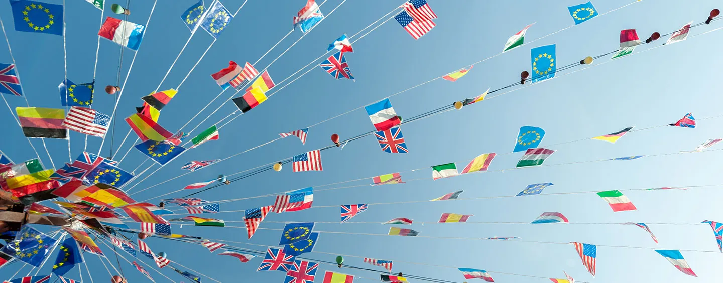 converging international flags against blue sky, Adobe Stock