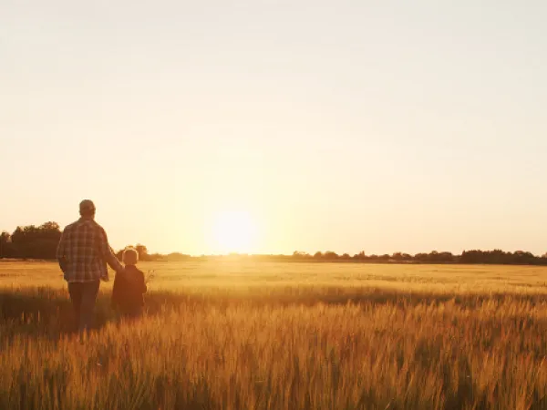 Farmer and son in a field at sunset. Image courtesy of Adobe Stock. 