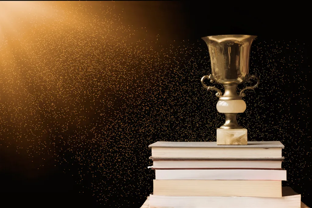 Golden trophy on pile of books, against blackboard, with sun rays. Courtesy of Adobe Stock. 