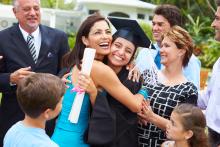 Student in graduation cap and gown surrounded by family and hugging a family member. Image courtesy of Getty Images.