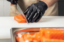 A gloved chef cuts salmon fillets on a large white cutting board. Courtesy of Adobe Stock. 