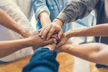 A group of colleagues showing teamwork by making a pile of hands. Courtesy of Adobe Stock. 
