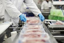 A person in personal protective equipment prepares meat in a processing plant. Image courtesy of Getty Images.
