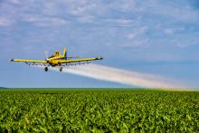 airplane spraying pesticides over field of crops